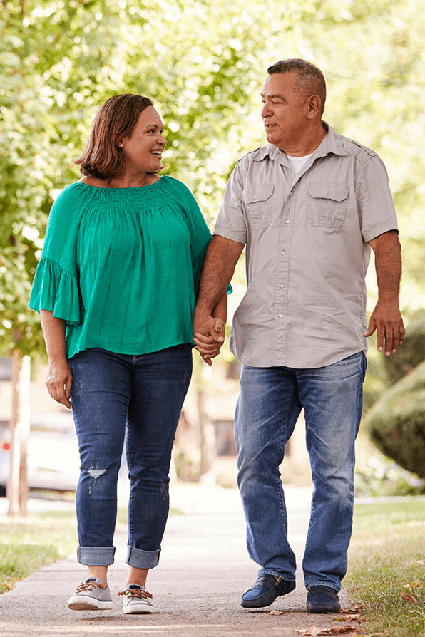 Couple holding hands and walking on a well-maintained concrete sidewalk in the park